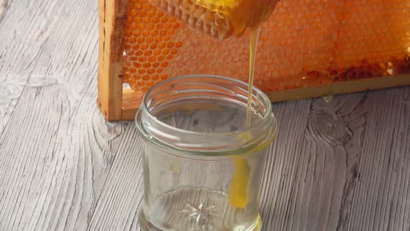 Closeup of the Fresh Honey Flowing Into the Glass Jar From the Honeycombs alt