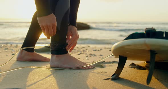 Low section of mid-adult caucasian male surfer tying surfboard leash at the beach 4k alt