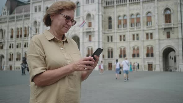 Senior Woman Using Cellphone By Parliament of Budapest Hungary alt