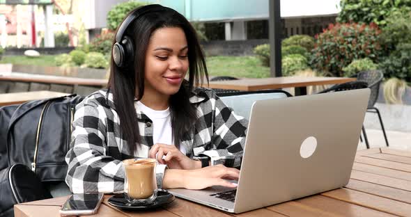Happy young black woman make video call online chat look at laptop screen sit in cafe.