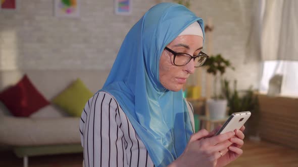 Portrait Young Muslim Woman in Hijab with a Scar From a Burn on Her Face Uses a Smartphone alt