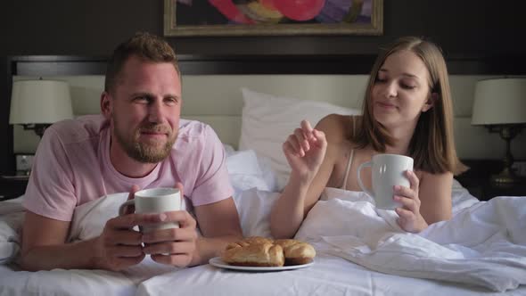 Man and Woman Are Eating Croissants with Coffee Lying in Bed in Morning alt