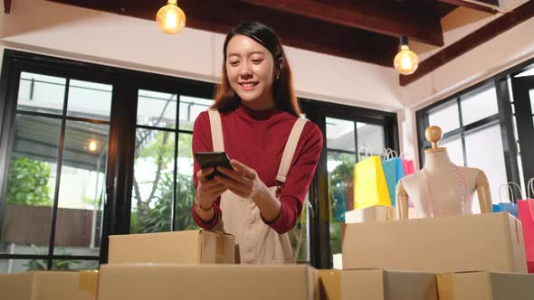 Asian woman use mobile phone to take a picture of banner on top of many boxes during delivery