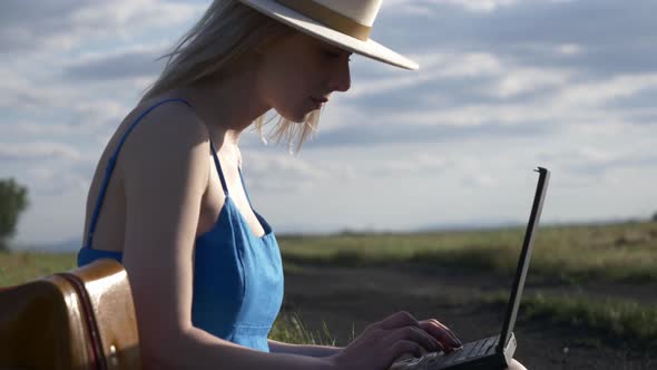 Girl in blue dress with laptop computer sit on country road in summer.