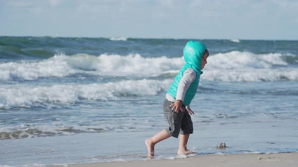 Toddler Boy in Waistcoat Is Playing with Sand on Sea Side. alt
