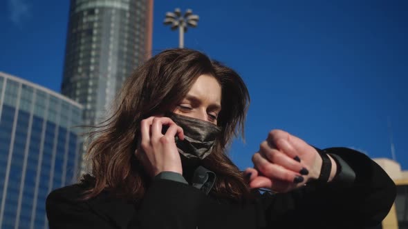 Brunette Girl in Antibacterial Mask Talks on the Phone and Looks at the Clock