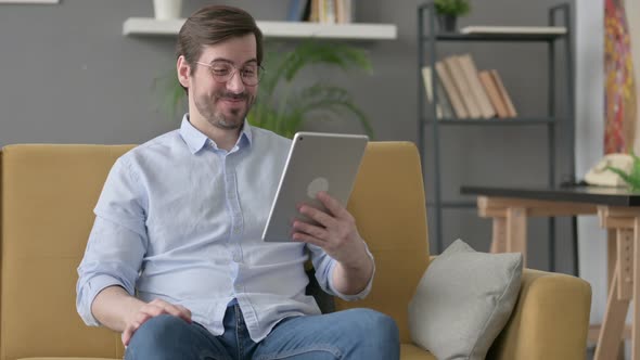Young Man Talking on Video Call on Tablet on Sofa alt
