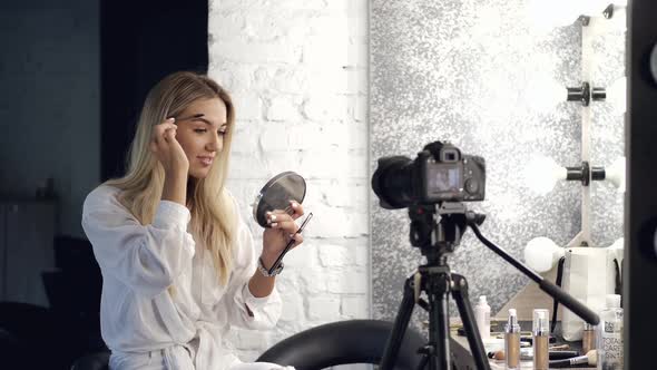 The Pretty Blond Makeup Artist Is Brushing Eyebrows Looking in a Mirror alt