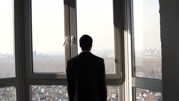 Young Successful Businessman Standing in Front of Windows Looking Into Distance on the City