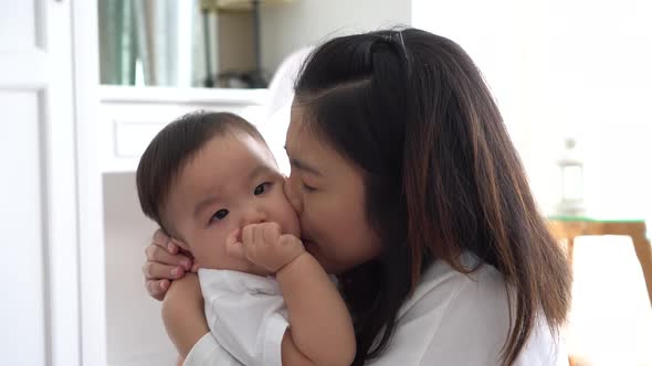 Asian Young Adult Mother Kissing Joyful Son in Living Room alt