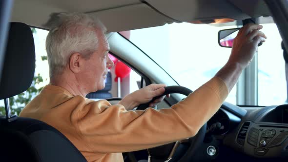 Senior Man Adjusts Rear-view Mirror Inside the Car