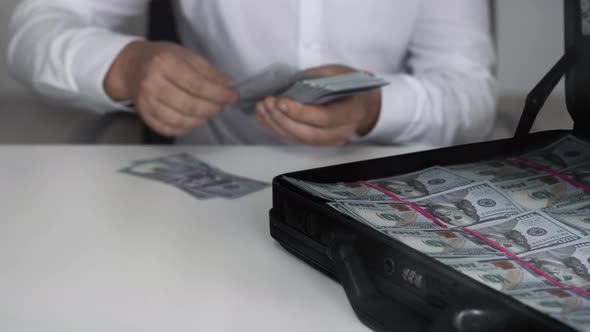 Man Counts the Cash Money Next To the Opened Case Full of Dollars. Bribe, Corruption Concept. Mafia alt