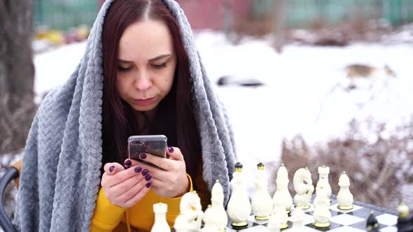 Young Woman Playing Chess and Browsing Smartphone in Yard alt