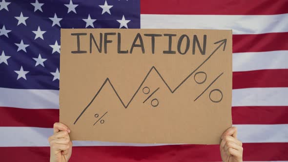 Hands Raise a Sign That Says Inflation and Graph Upward Against the Background of the American Flag alt