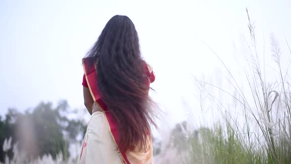 An Indian woman in saree with beautiful long and curly hair sways and moves her hair in a field, slo alt