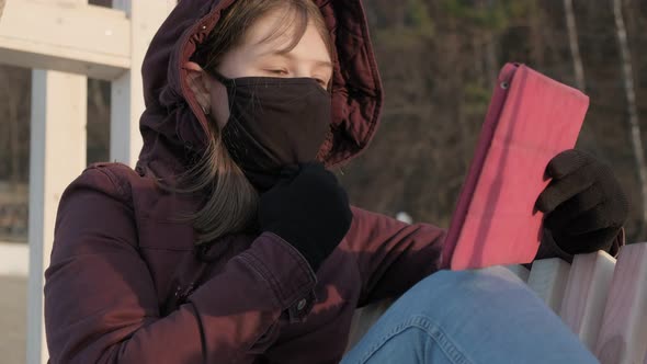 Girl in a Mask Outdoors Uses a Tablet. Insulation