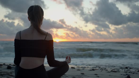 Young Woman Meditates on the Seashore Against the Background of Sunset
