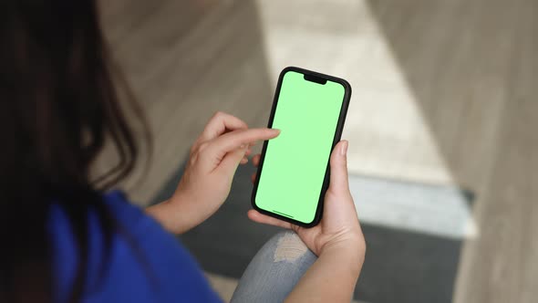 Woman Using Smartphone in Vertical Mode with Green Mock-up Screen Doing Scrolling Gestures