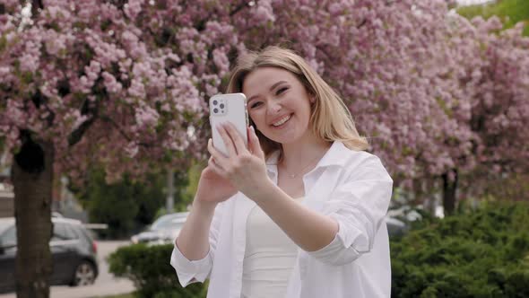 Beautiful Blonde Woman Has Videocall By Smartphone in the City Park