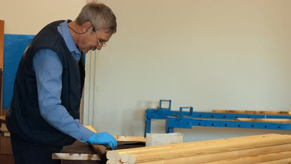 An Elderly Carpenter with Glasses Varnishes Wooden Boards in a Carpenter's Shop alt