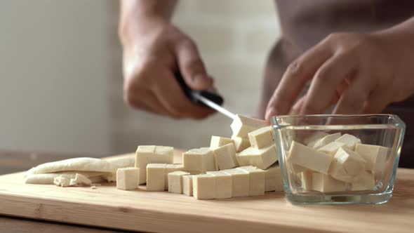 Chef hands placing and dropping tofu cubes into glass bowl