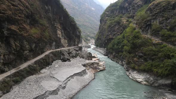 Flying through canyon over the Marsyangdi River with dirt road cut in the cliffs alt
