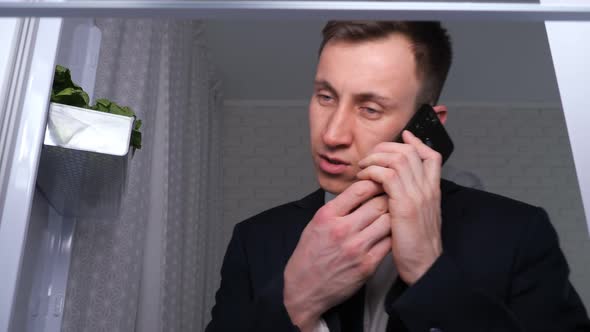 Man Talks on Phone Eating Sandwich with Butter Near Fridge alt
