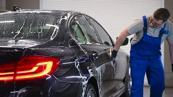 Car Detailing the Man Washes Backlights of a Car with a Hand Covered with a Special Wash Glove