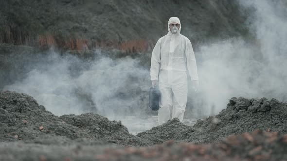 Lab technician in a mask and chemical protective suit walking on dry ground alt