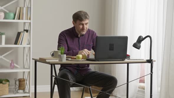 Wide Shot of Handsome Confident Middle Aged Man Adjusting Hair and Pointing at Laptop alt