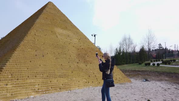 Girl Takes a Photo Near a Small Egyptian Pyramid. Park of Miniatures. alt