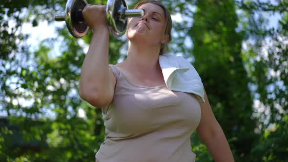 Portrait of Plussize Sportswoman Screaming Lifting Heavy Dumbbell in Slow Motion Outdoors alt