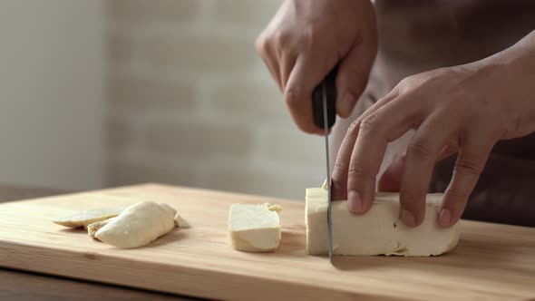 Hands of chef cutting raw tofu block on wood cutting board