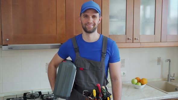 Repairman Holds a Suitcase of Tools in the Kitchen and Looks at the Camera alt