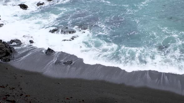 Whitewash waves rolling and breaking on black sand beach in remote bay in capital Wellington, New Ze alt