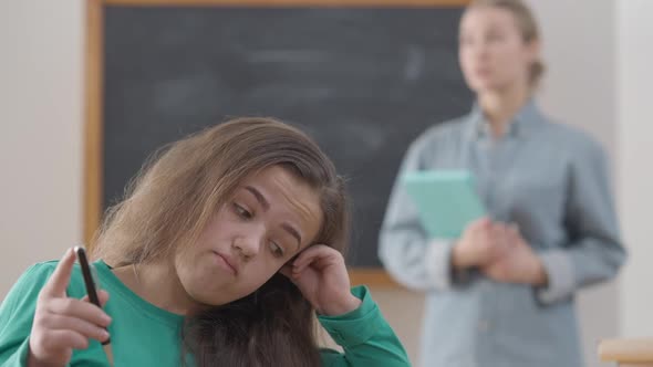 Closeup Bored Sad Little Person Sitting at Desk in College with Blurred Lecturer Talking at alt