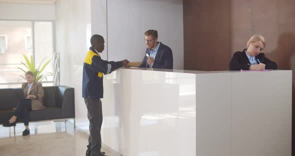 Man Secretary Signing for Delivered Padded Envelope at Reception Desk in Office Building alt