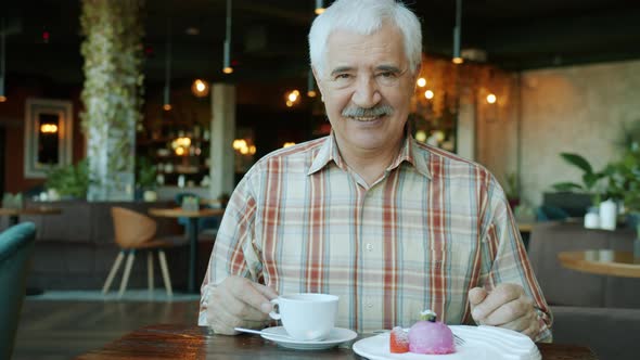 Portrait of Good-looking Senior Man Smiling Sitting at Table in Restaurant alt