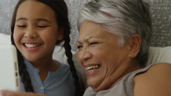 Grandmother and granddaughter using digital tablet in bed room alt