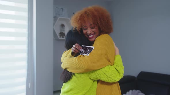 Multiracial Lesbian Couple Expecting Baby. Embracing with Ultrasound Baby Picture alt