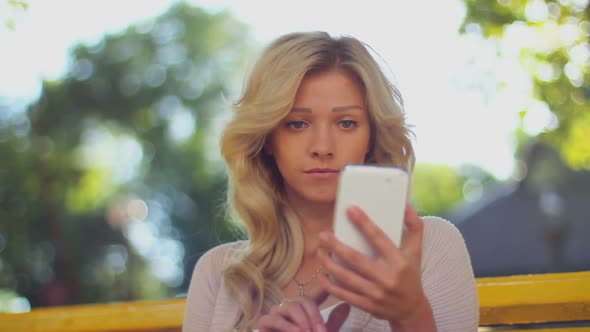 Young Woman Typing Sms and Taking Photo of Herself in Park Bench alt