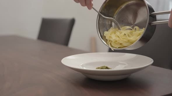 Slow Motion Man Pour Pesto Fettuccine From Saucepan To White Pasta Plate on Walnut Table alt