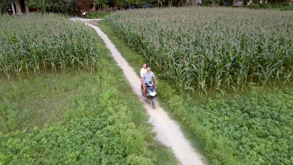 Couple Rides Scooter Between Fields on Spring Day Aerial alt