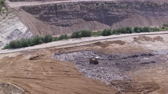 Birds fly aroud garbage pile on junkyard near working excavator. Aerial shot. 4K