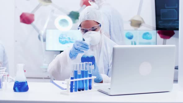 Female Scientist Looking at Reactive Blue Solution and Writing Formula alt