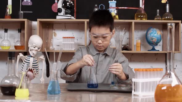 School Laboratory Experience in a Chemistry Lesson Asian Boy in Protective Glasses Pours a Blue alt