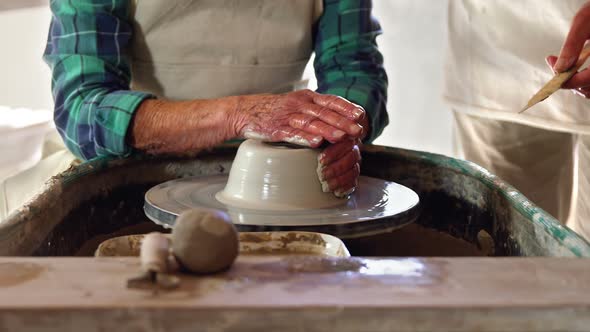 Mid-section of male potter assisting female potter alt