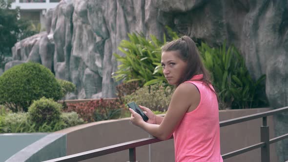 Young Brown Haired Girl Stands Outside Holding Mobile Phone alt