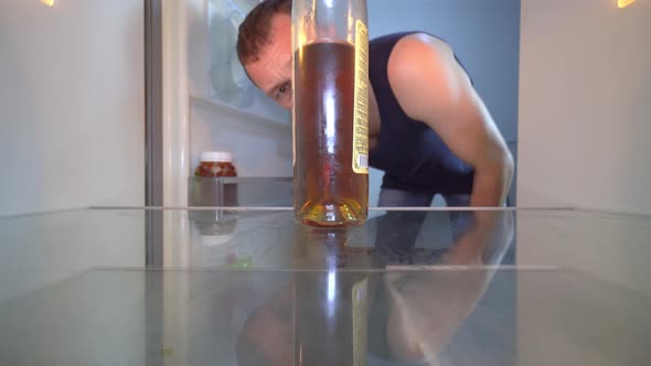 man looks into an empty refrigerator and takes out bottle of alcohol. Alcoholism alt