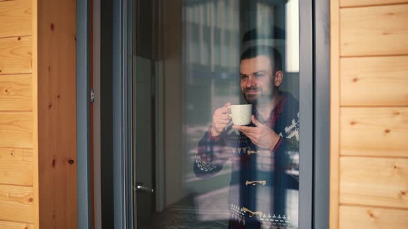 Man Drinking Tea or Coffee Near the Window and Looking Through the Glass alt